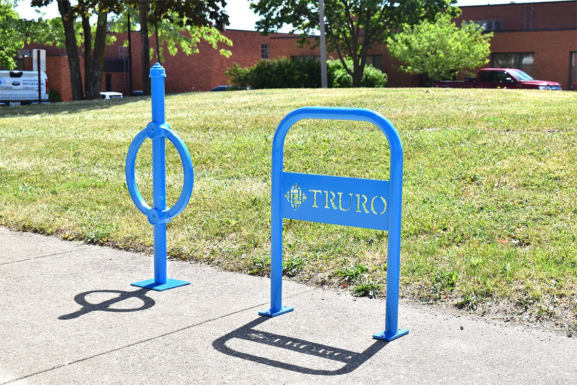Blue commercial bike racks installed on a sidewalk, including a custom branded Truro bike rack for secure public bicycle parking.